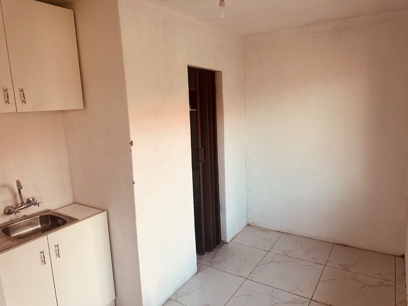 A compact, empty kitchen area featuring basic built-in cabinetry, a stainless steel sink, and tiled flooring, ready for renovation or staging.