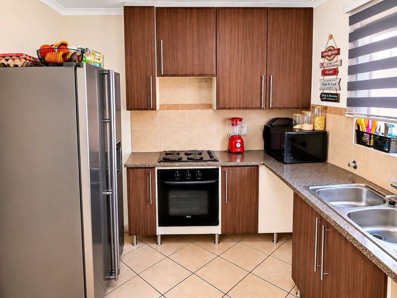 A functional kitchen featuring dark wood cabinetry, granite countertops, a built-in oven with electric hob, and a double basin stainless steel sink.