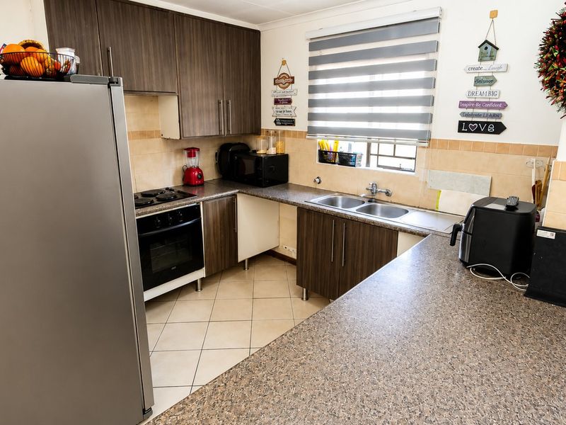 A functional kitchen featuring dark wood-look cabinetry, laminate countertops, a double bowl sink, and a built-in oven with hob.