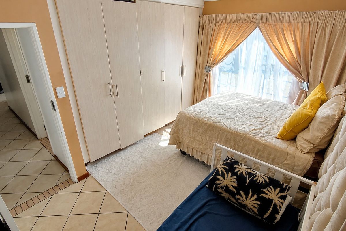 A bedroom featuring built-in cupboards, tiled flooring, and natural light through a window with curtain rails.