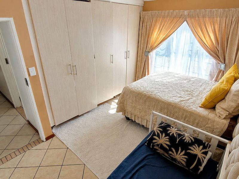 A bedroom featuring built-in cupboards, tiled flooring, and natural light through a window with curtain rails.