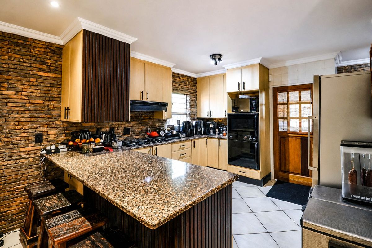 A functional kitchen featuring granite countertops, timber cabinetry, built-in appliances, and a distinctive stone veneer feature wall with a breakfast bar.
