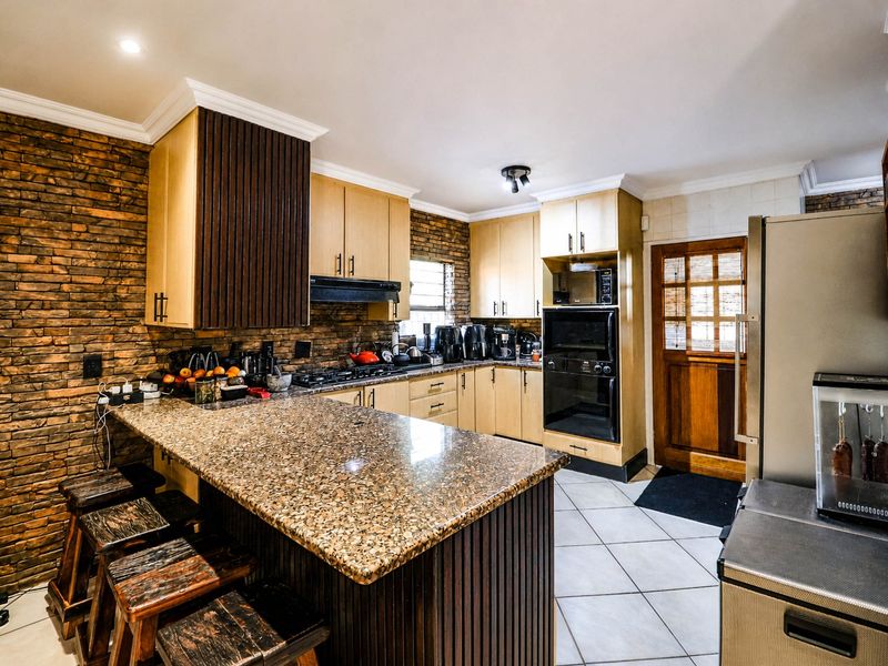 A functional kitchen featuring granite countertops, timber cabinetry, built-in appliances, and a distinctive stone veneer feature wall with a breakfast bar.