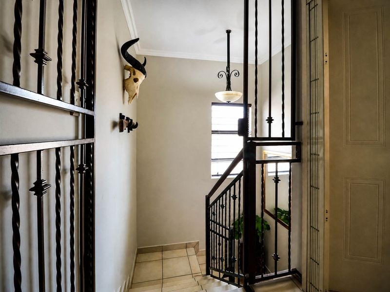 A bright hallway featuring tiled flooring, a decorative pendant light, and secure wrought iron gates leading to a staircase.