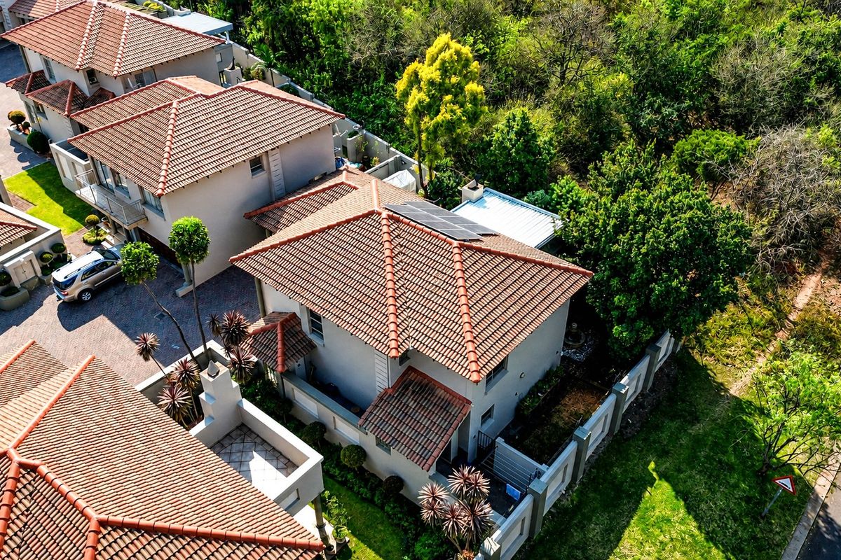 Aerial view of a residential property featuring a tiled roof with solar panels, a paved driveway, and established garden surroundings within a secure complex.