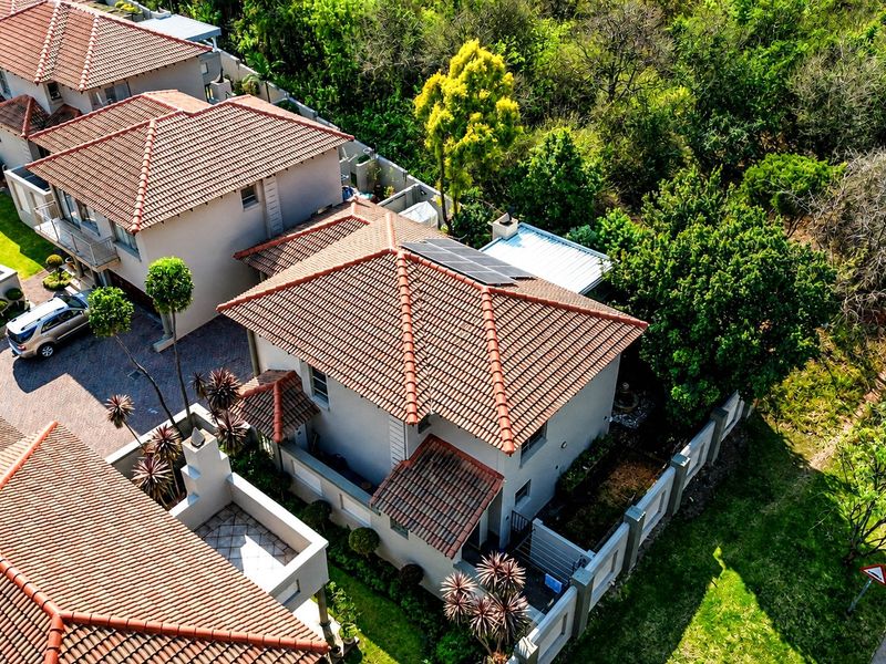 Aerial view of a residential property featuring a tiled roof with solar panels, a paved driveway, and established garden surroundings within a secure complex.