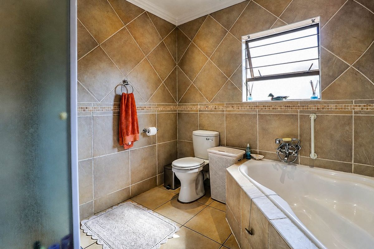 A functional bathroom featuring tiled walls and flooring, a built-in bathtub, a toilet, and a separate shower enclosure with a louvered window.