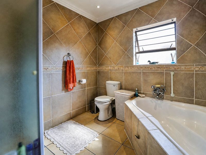 A functional bathroom featuring tiled walls and flooring, a built-in bathtub, a toilet, and a separate shower enclosure with a louvered window.