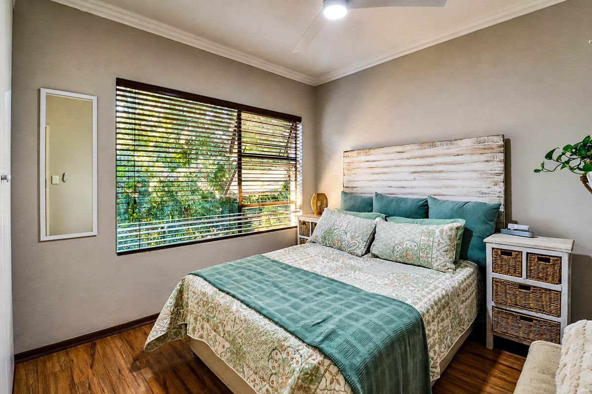 A well-maintained bedroom featuring laminate flooring, a ceiling fan, and large windows with venetian blinds, offering a bright and comfortable living space.