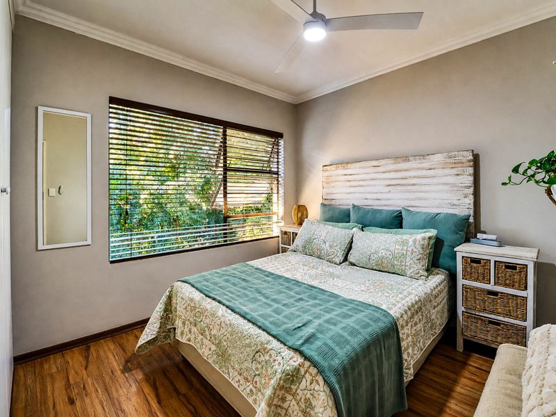 A well-maintained bedroom featuring laminate flooring, a ceiling fan, and large windows with venetian blinds, offering a bright and comfortable living space.