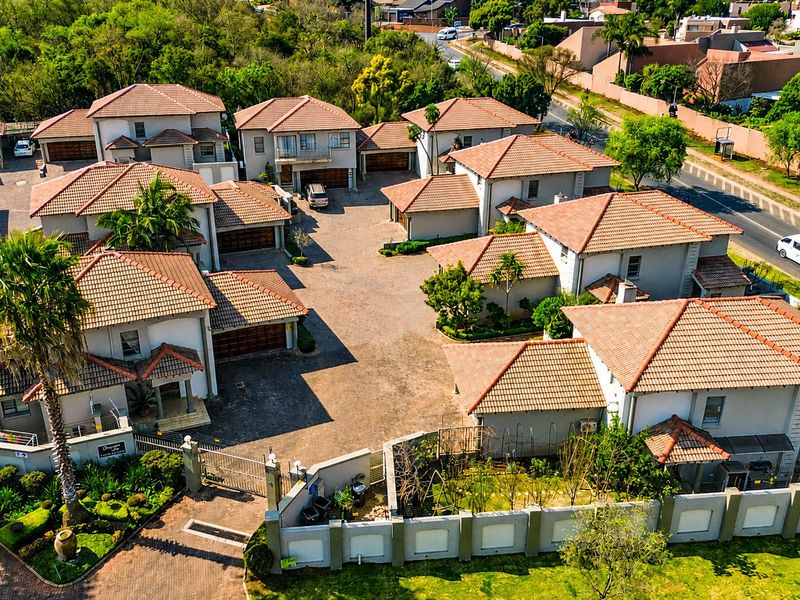 Aerial view of a residential complex featuring multiple houses with tiled roofs, paved driveways, and secure perimeter walling.
