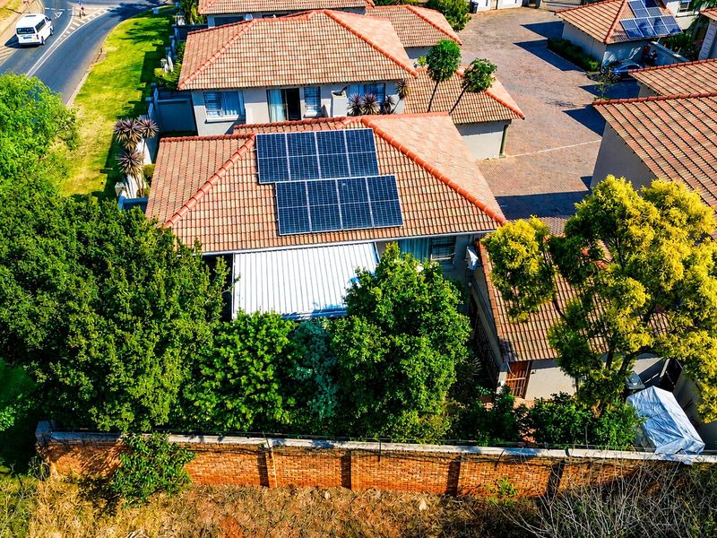 Aerial view of a residential property featuring a tiled roof with installed solar panels, a covered patio, and a brick boundary wall.