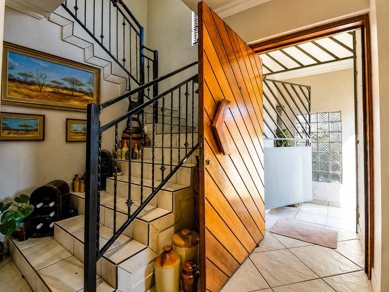 Welcoming entrance hall featuring a striking timber pivot door, tiled staircase with wrought iron railing, and natural light through glass block windows.
