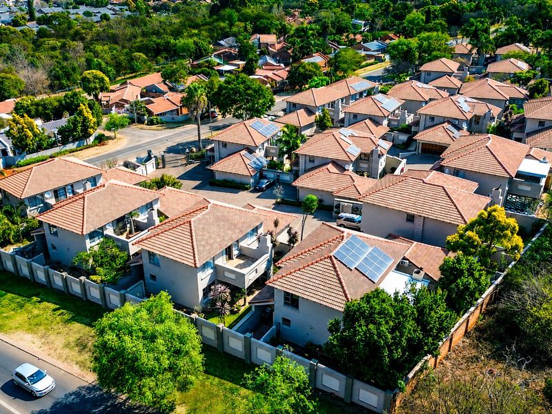 Aerial view of a residential estate featuring multiple houses with tiled roofs, solar panel installations, and perimeter walling.