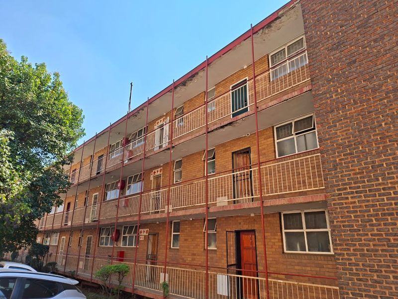 Exterior view of a multi-story apartment building featuring face brick construction, external metal walkways, and security gates on individual unit entrances.