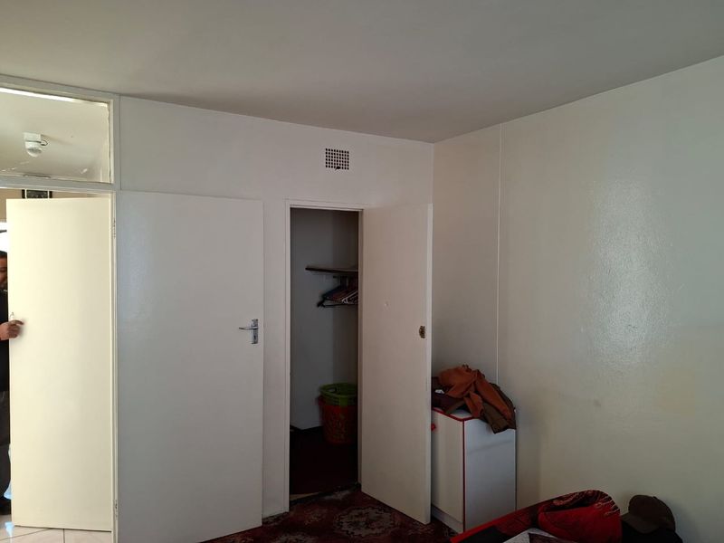 A bedroom interior featuring a built-in closet with open shelving and a ventilation grille, finished with plain white walls.