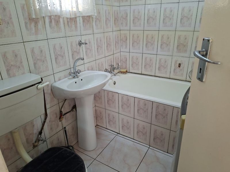 A compact bathroom featuring a pedestal basin, bathtub, and dated ceramic tiling throughout. The space offers a functional layout ready for modernization.