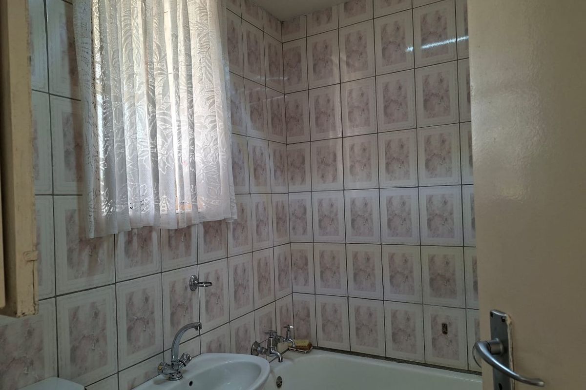 A dated bathroom featuring a standard bathtub, pedestal washbasin, and full-height ceramic wall tiling.
