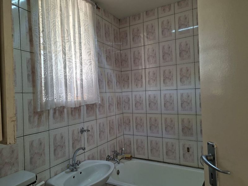 A dated bathroom featuring a standard bathtub, pedestal washbasin, and full-height ceramic wall tiling.