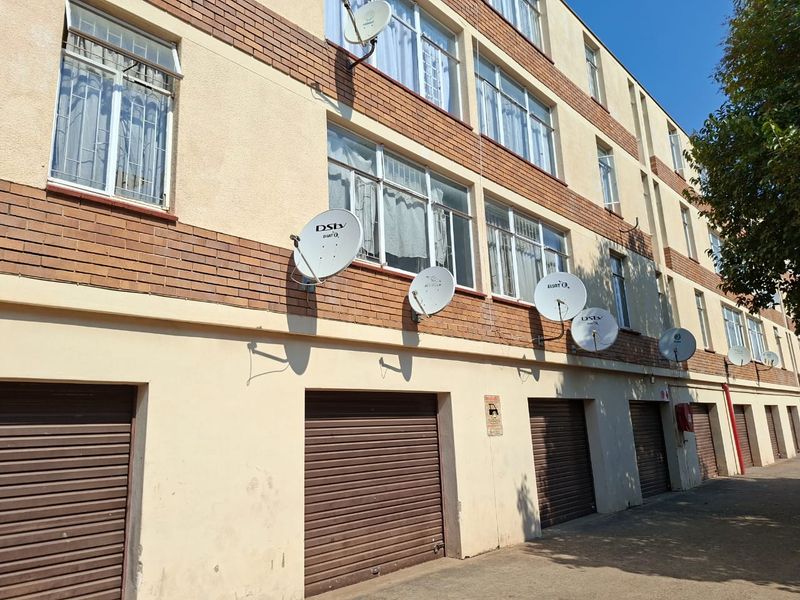 Exterior view of an apartment building featuring multiple roller shutter garage doors, brick and plaster facade, and mounted satellite dishes.