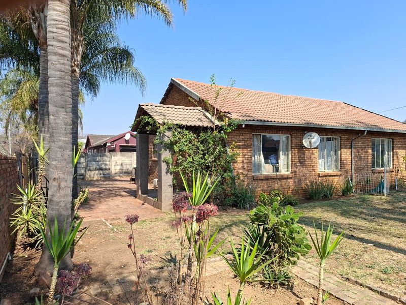 A single-story brick house featuring a tiled roof, a covered entrance porch, and a paved driveway, set within a garden with established landscaping.