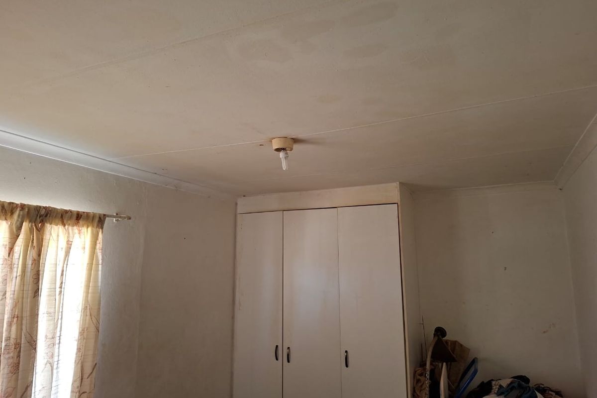 A bedroom featuring a built-in wardrobe and cove cornice, showing signs of ceiling water staining and general wear on the wall finishes.
