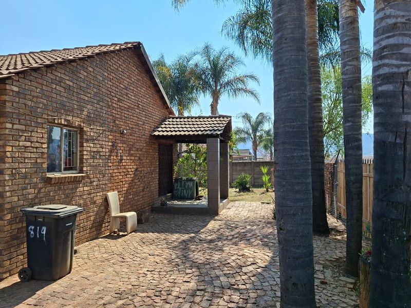 Rear exterior view of a brick house featuring a paved patio area, covered entrance, and established palm trees.