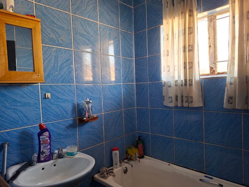 A functional bathroom featuring blue wall tiles, a standard bathtub, and a wall-mounted basin with a wooden-framed mirror.