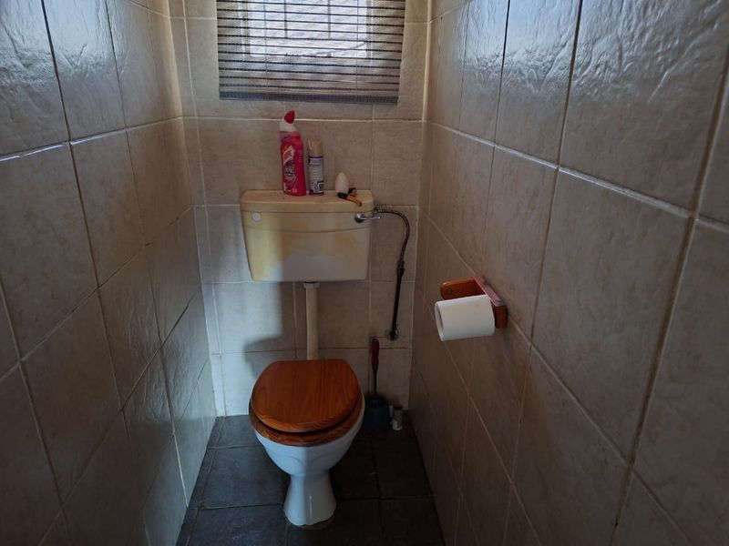A compact bathroom featuring fully tiled walls and floors, equipped with a standard toilet and wall-mounted toilet roll holder.