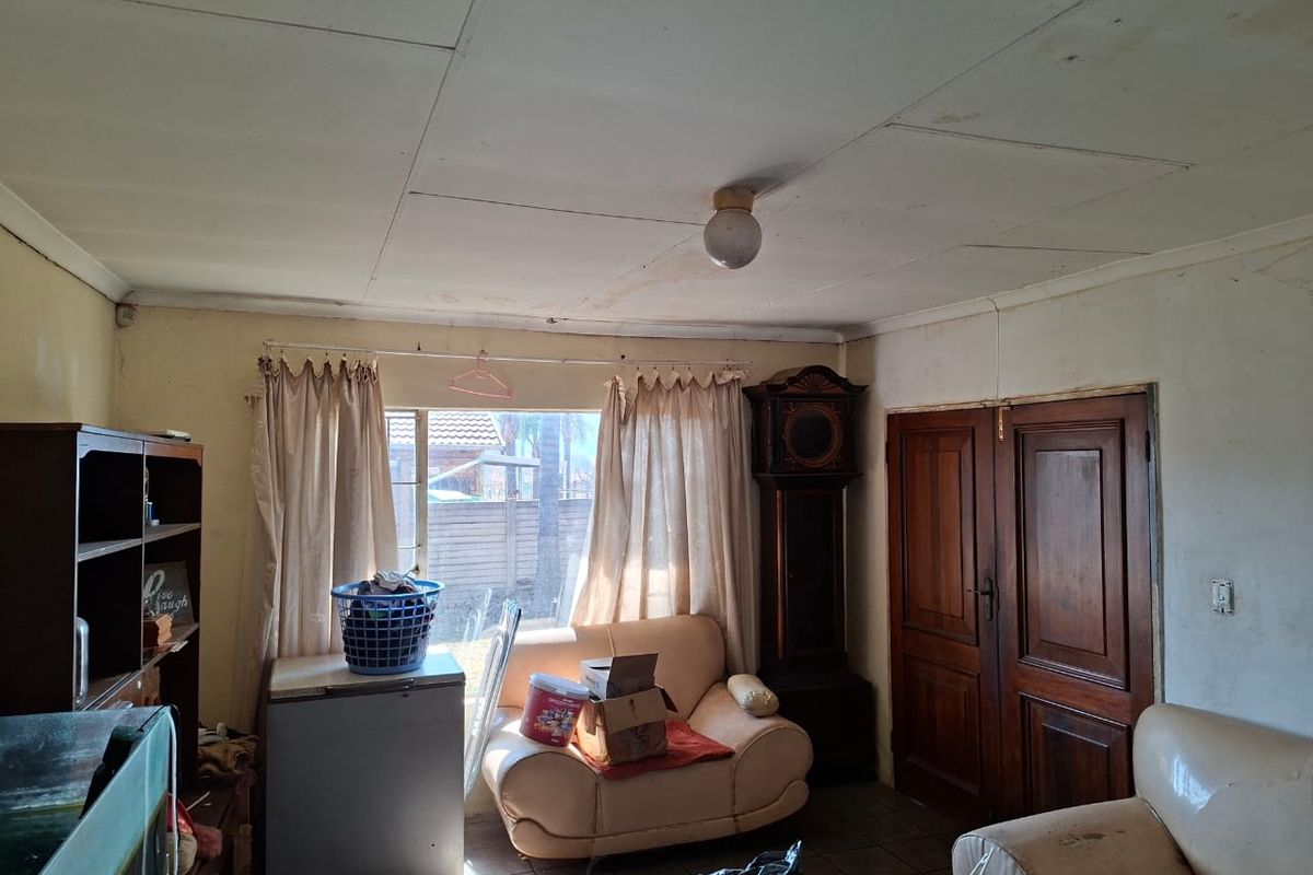 A living room featuring tiled flooring, double wooden doors, and ceiling-mounted lighting, currently requiring cosmetic updates and ceiling repairs.