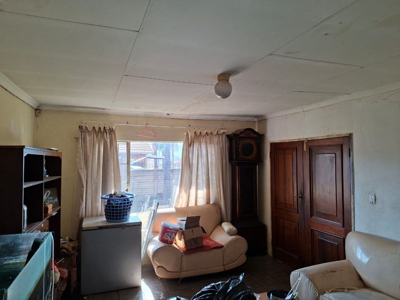 A living room featuring tiled flooring, double wooden doors, and ceiling-mounted lighting, currently requiring cosmetic updates and ceiling repairs.