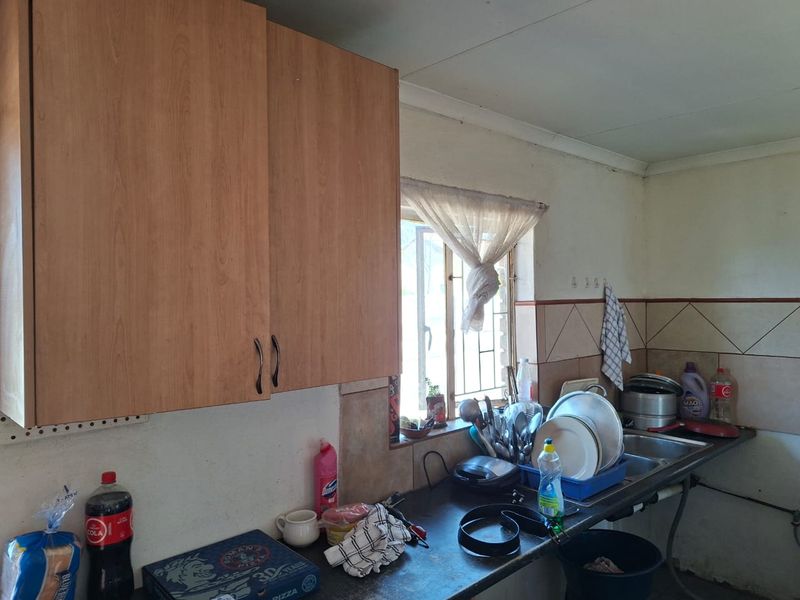 A functional kitchen area featuring laminate cabinetry, a stainless steel sink, and tiled backsplash, requiring cosmetic updates to modernize the space.