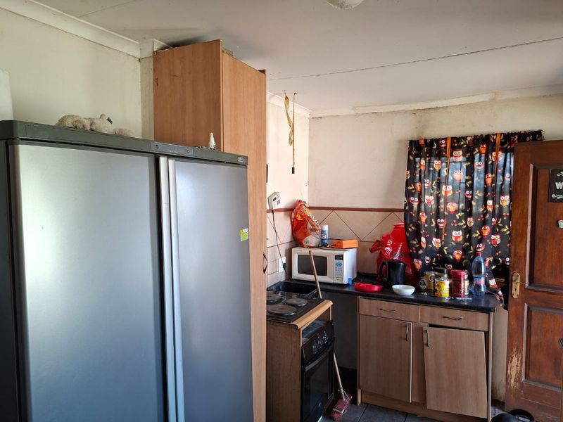A compact kitchen featuring built-in cabinetry, laminate countertops, and an electric stove, currently requiring cosmetic updates and maintenance to improve its overall condition.