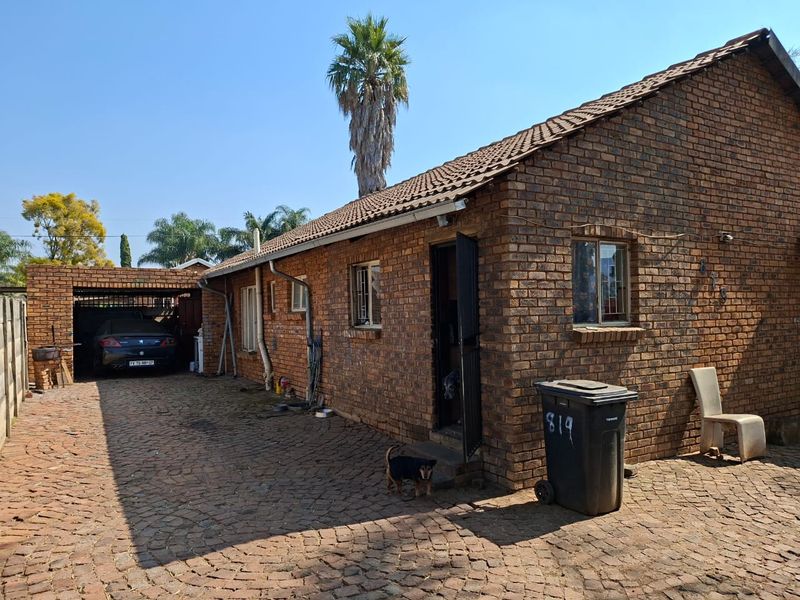 A single-story face brick house featuring a paved driveway, attached carport, and tiled roof, presenting a classic residential exterior.