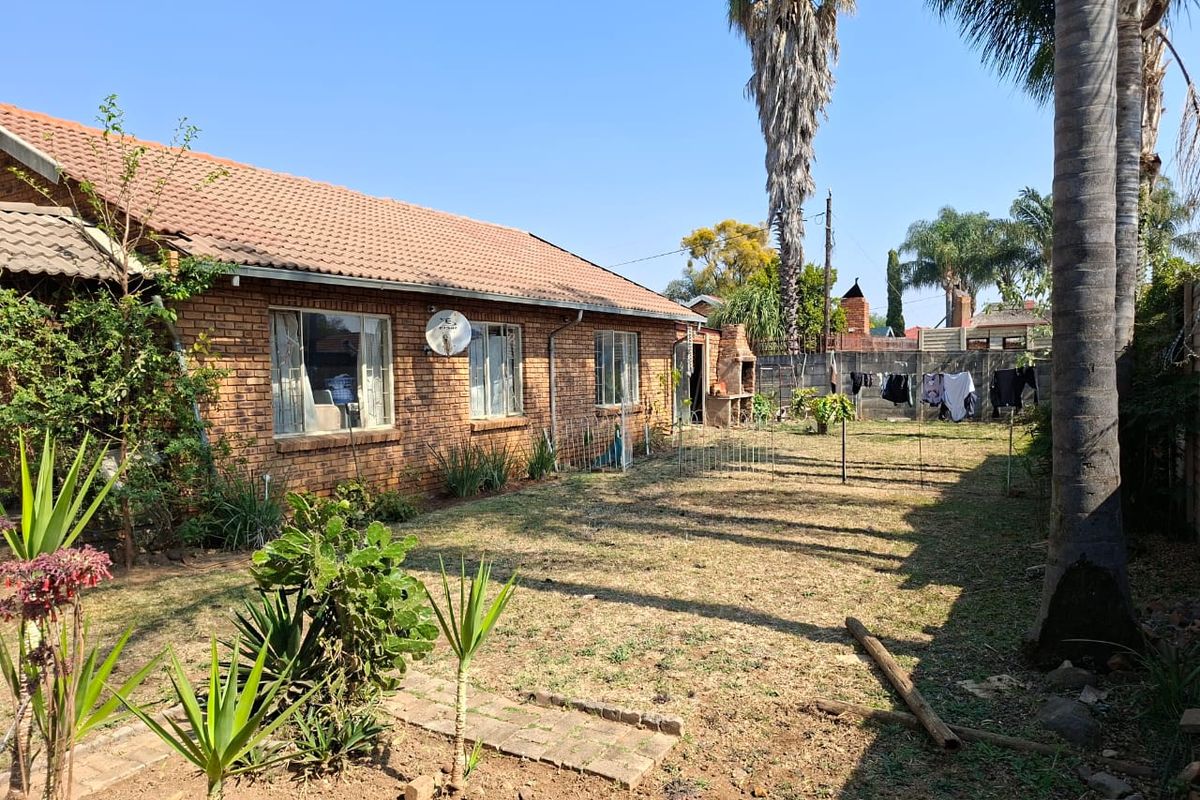 Rear view of a brick house featuring a tiled roof, a built-in outdoor braai area, and a spacious garden with boundary walling.