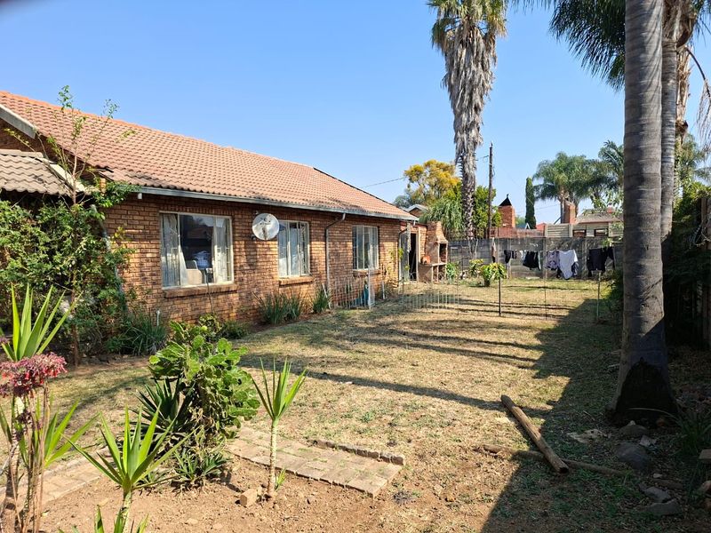 Rear view of a brick house featuring a tiled roof, a built-in outdoor braai area, and a spacious garden with boundary walling.