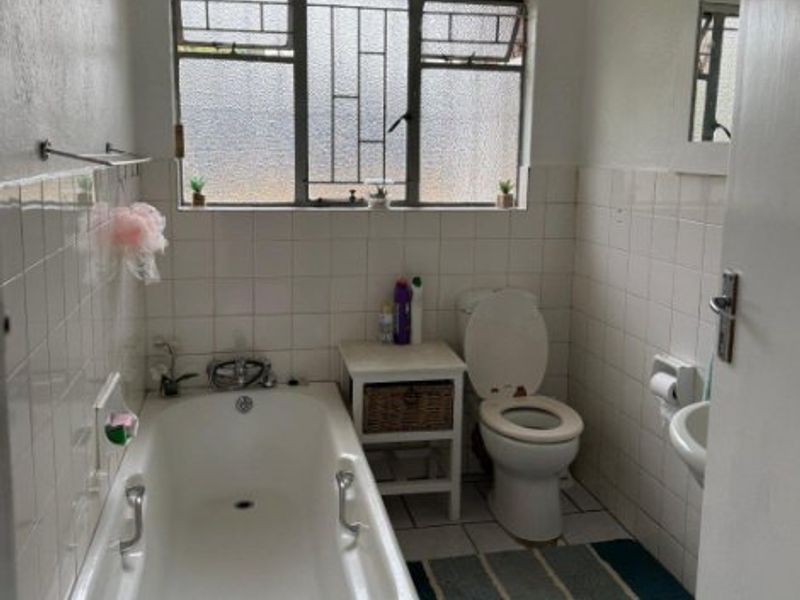 A functional bathroom featuring a bathtub, toilet, and wall-mounted basin with tiled finishes and a steel-framed window.