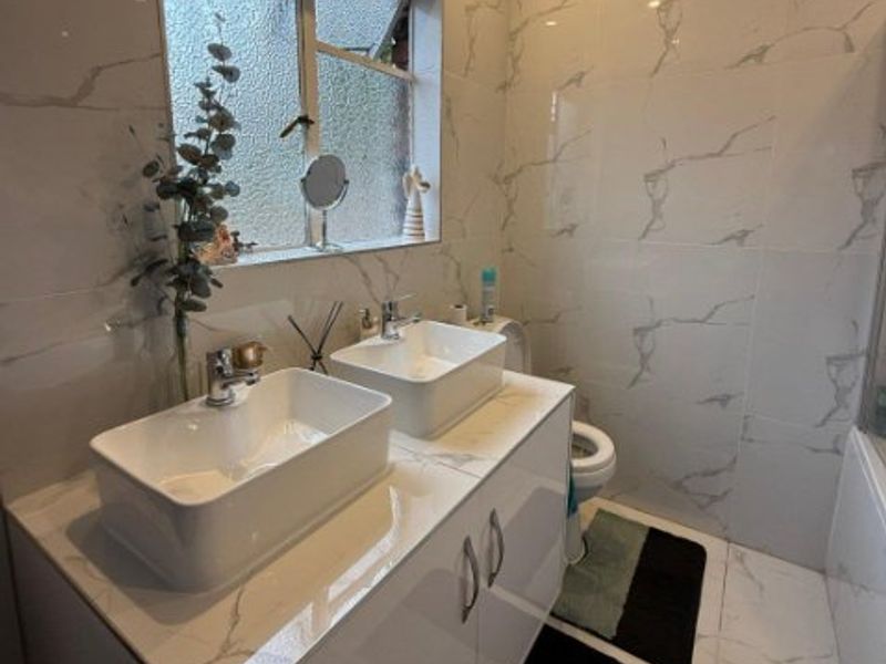 Modern bathroom featuring a double vanity with vessel sinks, marble-look wall and floor tiling, and recessed lighting.