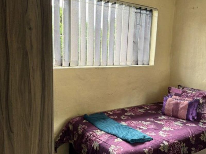 A compact bedroom featuring tiled flooring, vertical window blinds, and an integrated wall vent, requiring cosmetic updates to improve the overall finish.