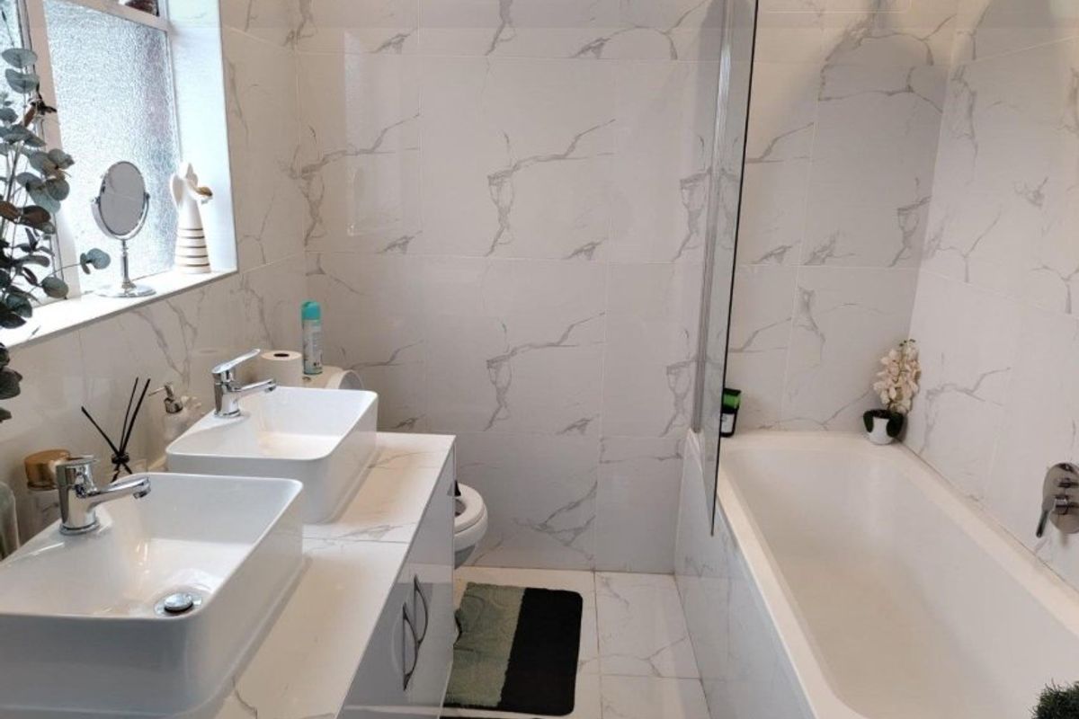 Modern bathroom featuring a double vanity with vessel sinks, a bathtub with a glass screen, and contemporary marble-effect tiling throughout.