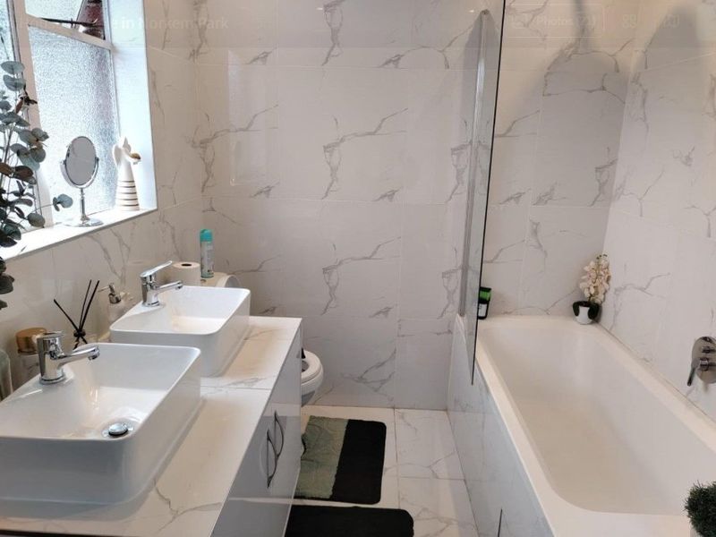 Modern bathroom featuring a double vanity with vessel sinks, a bathtub with a glass screen, and contemporary marble-effect tiling throughout.