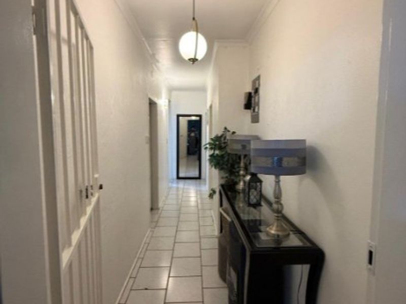 A clean, well-lit hallway featuring tiled flooring, cove cornicing, and a central pendant light fixture, providing a functional transition space within the home.