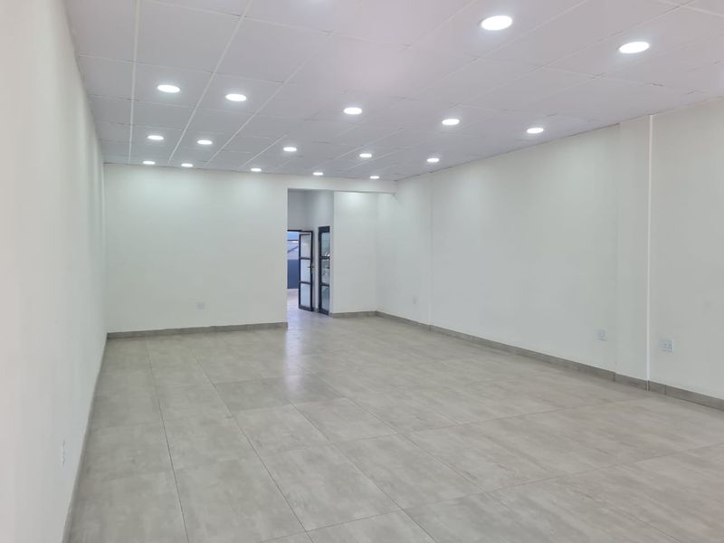 A bright, open-plan commercial office space featuring modern tiled flooring, a suspended ceiling with recessed downlights, and neutral wall finishes.
