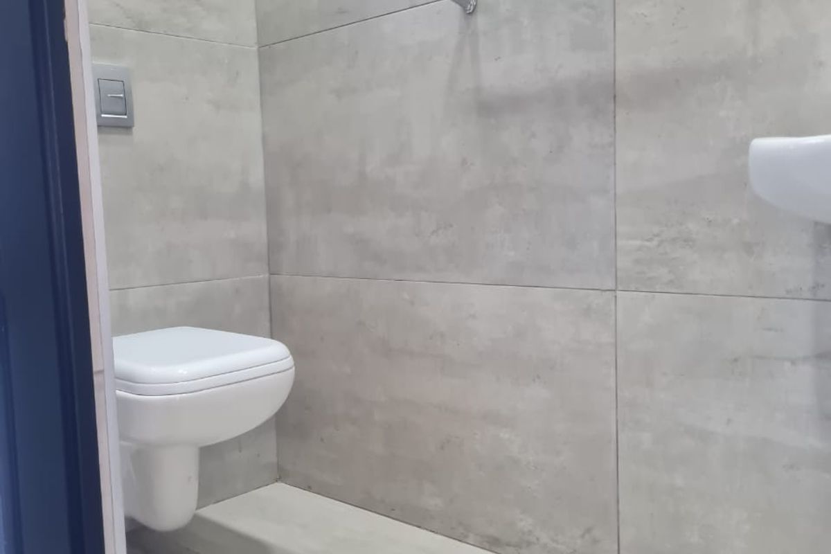 A modern, minimalist bathroom featuring large format grey wall tiles, a wall-mounted toilet, and a wall-mounted basin.