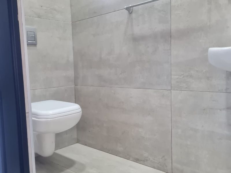 A modern, minimalist bathroom featuring large format grey wall tiles, a wall-mounted toilet, and a wall-mounted basin.