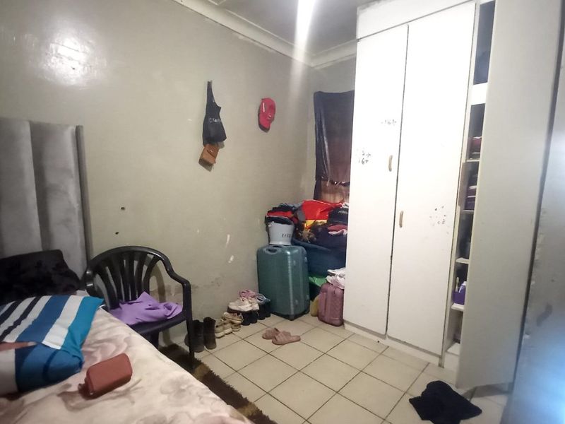 A bedroom featuring tiled flooring and a built-in wardrobe, requiring cosmetic updates to the wall finishes and general maintenance.