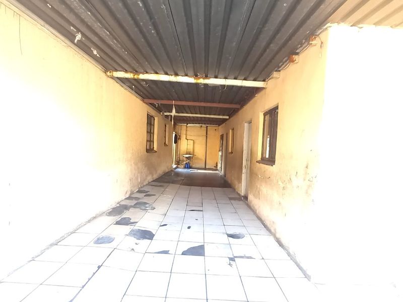 A covered outdoor walkway or patio area featuring tiled flooring and a corrugated metal roof, showing significant signs of wear and maintenance requirements.