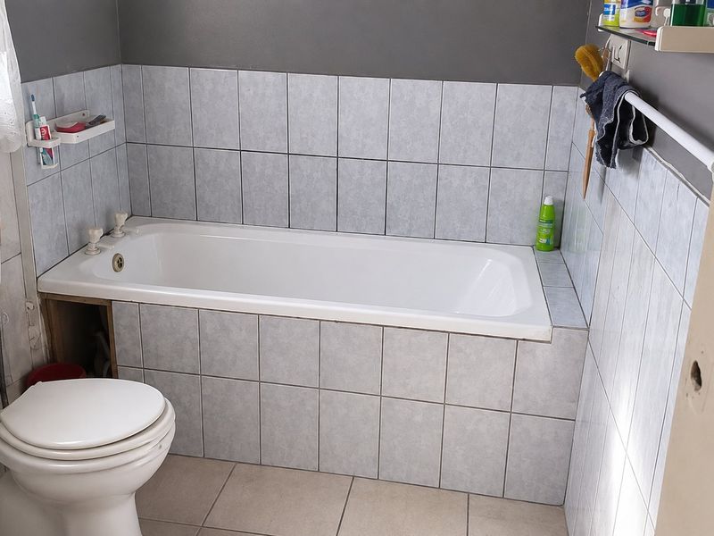 A functional bathroom featuring a built-in bathtub with tiled surround, a standard toilet, and neutral wall and floor tiling.