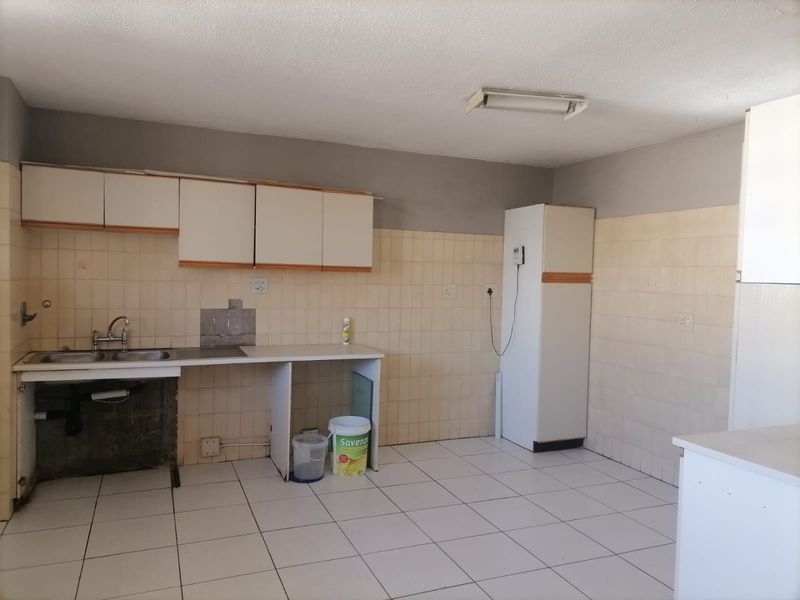 A functional kitchen space featuring tiled flooring, a stainless steel sink, and built-in cabinetry, currently awaiting updates to modernize the finishes.