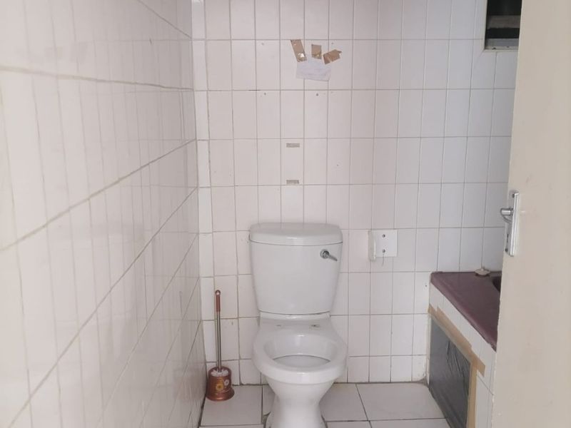 A compact bathroom featuring white wall and floor tiles, a standard toilet, and a vanity unit requiring finishing touches.